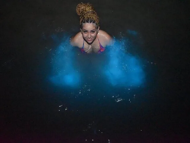 Une femme nage dans une eau bioluminescente bleu lumineux au Luminous Lagoon.