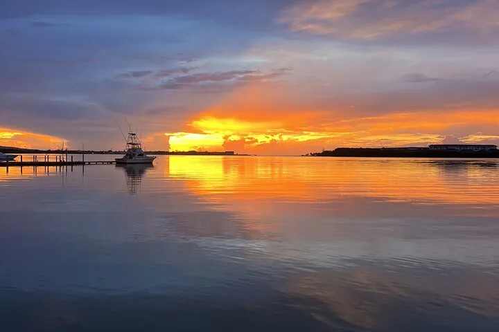 Un coucher de soleil orange éclatant au-dessus de l’eau, avec des bateaux au loin.